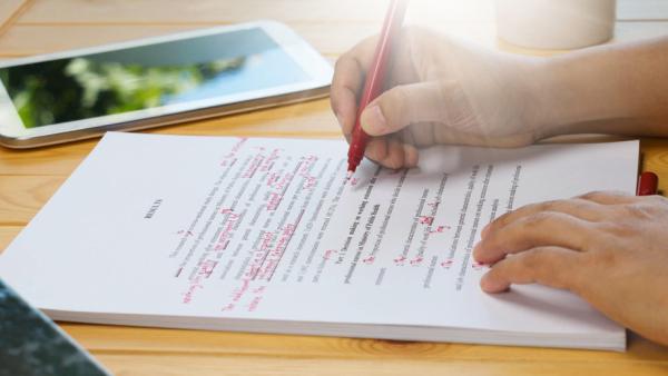 person editing a manuscript with a red pen